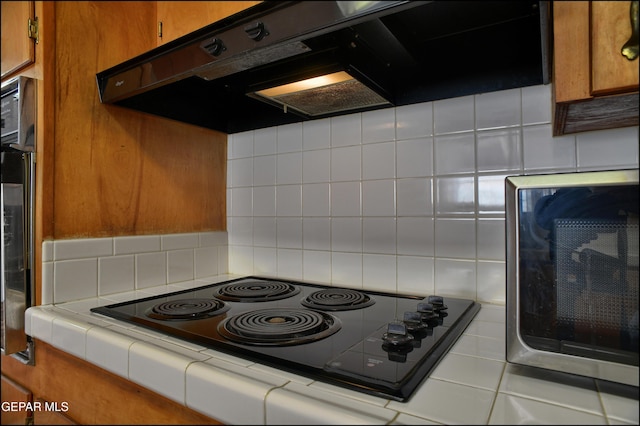 kitchen featuring ventilation hood, tile counters, tasteful backsplash, and black stovetop