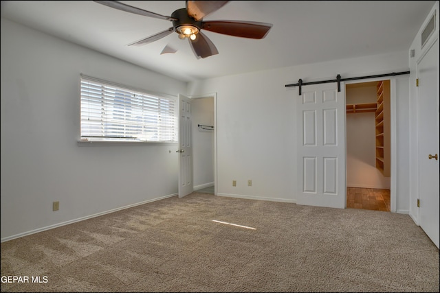 unfurnished bedroom with a spacious closet, ceiling fan, a barn door, and carpet floors