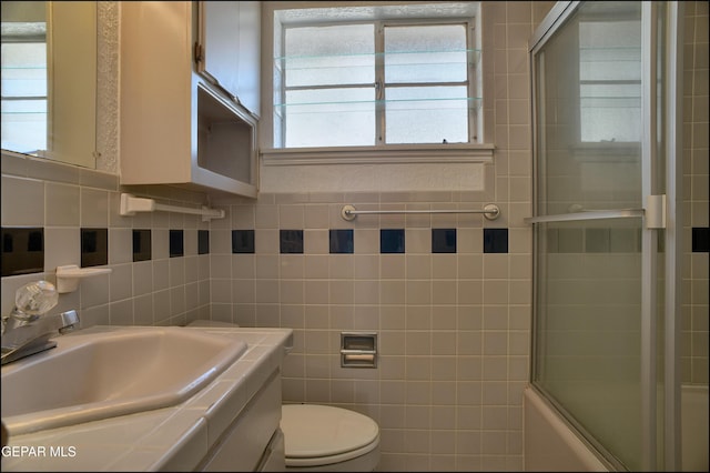 full bathroom featuring shower / bath combination with glass door, vanity, toilet, and tile walls