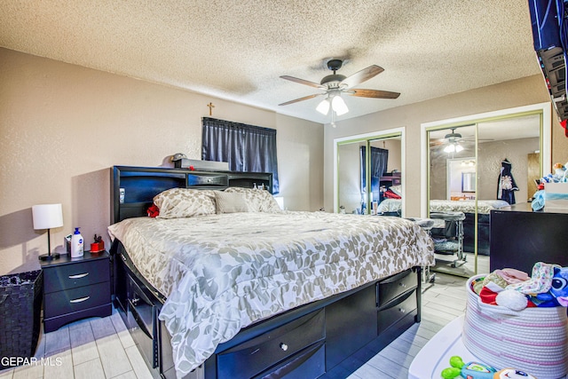 bedroom with a textured ceiling, light hardwood / wood-style flooring, ceiling fan, and multiple closets