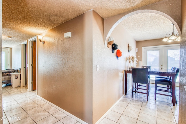 corridor featuring french doors, a textured ceiling, light tile patterned floors, and a notable chandelier