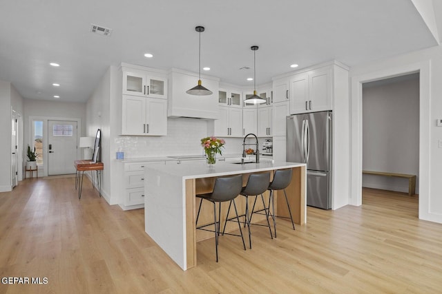 kitchen featuring white cabinets, stainless steel fridge, light hardwood / wood-style floors, and a center island with sink