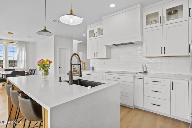 kitchen with white cabinetry, sink, premium range hood, pendant lighting, and a kitchen island with sink