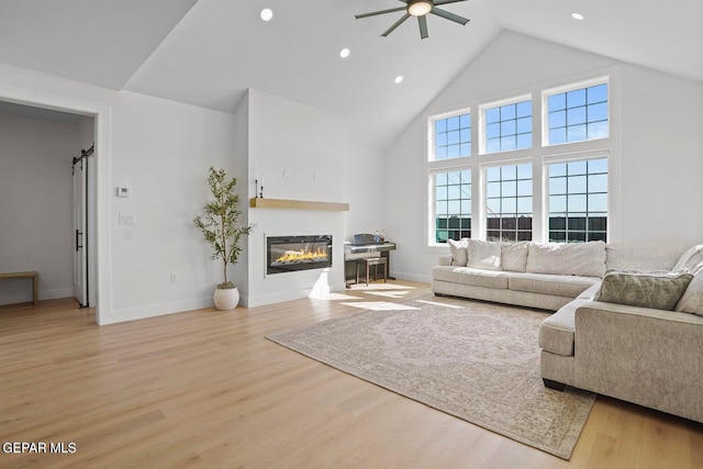 living room featuring ceiling fan, a barn door, high vaulted ceiling, and light hardwood / wood-style flooring