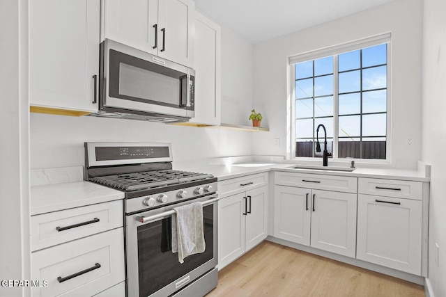 kitchen with white cabinets, sink, light wood-type flooring, and stainless steel appliances