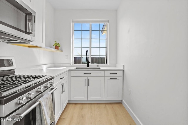 kitchen with appliances with stainless steel finishes, light hardwood / wood-style flooring, white cabinetry, and sink