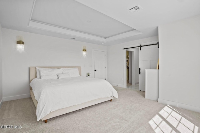 carpeted bedroom featuring a barn door and a raised ceiling