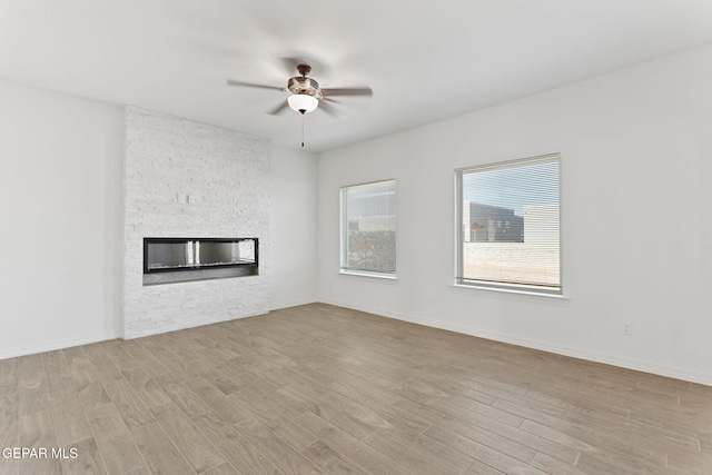 unfurnished living room with ceiling fan, a stone fireplace, and light wood-type flooring