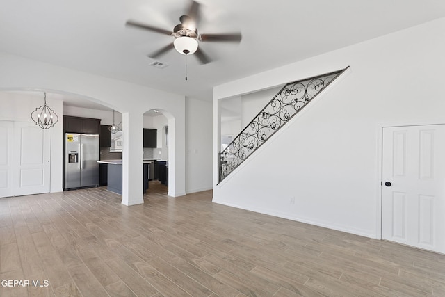 unfurnished living room featuring ceiling fan with notable chandelier and light hardwood / wood-style floors