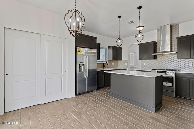 kitchen with a center island, wall chimney range hood, tasteful backsplash, light hardwood / wood-style floors, and appliances with stainless steel finishes