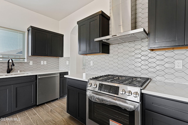 kitchen with tasteful backsplash, wall chimney exhaust hood, stainless steel appliances, sink, and hardwood / wood-style flooring