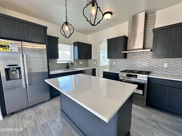 kitchen featuring wall chimney exhaust hood, a kitchen island, decorative light fixtures, and appliances with stainless steel finishes