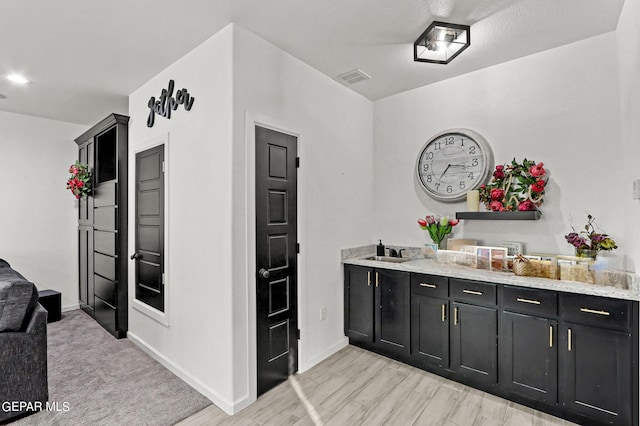 bar featuring light stone counters, light colored carpet, and sink