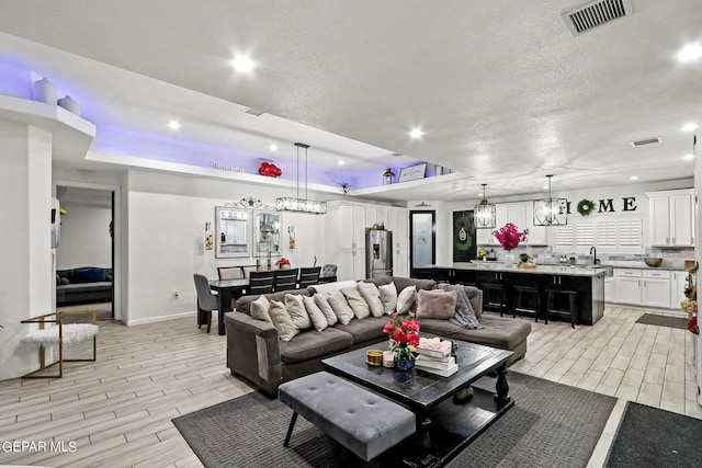 living room with sink, light hardwood / wood-style flooring, a textured ceiling, and a notable chandelier