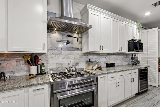 kitchen featuring light stone countertops, wall chimney exhaust hood, stainless steel appliances, beverage cooler, and white cabinets