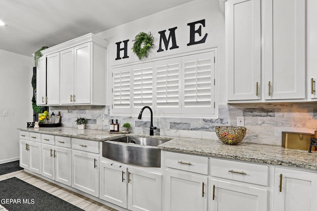 kitchen featuring sink, tasteful backsplash, light stone counters, white cabinets, and light wood-type flooring