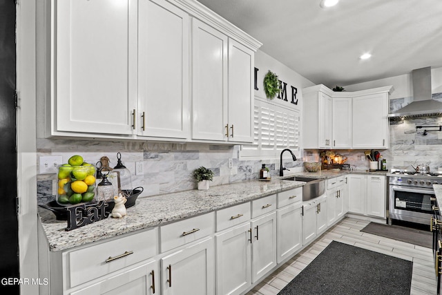 kitchen with stainless steel stove, white cabinetry, wall chimney exhaust hood, and sink