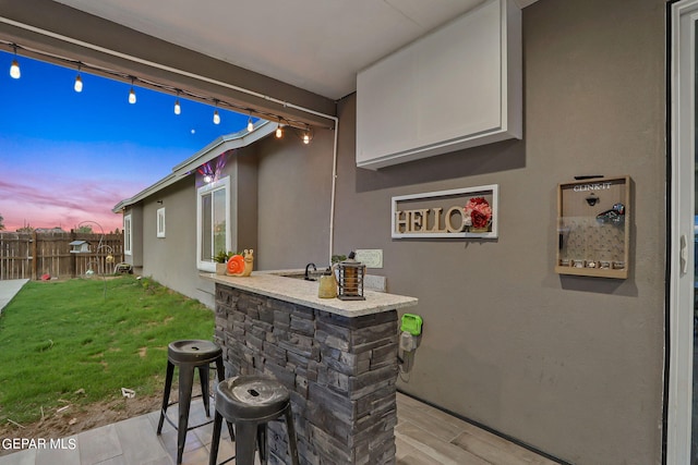 patio terrace at dusk featuring a lawn and a bar