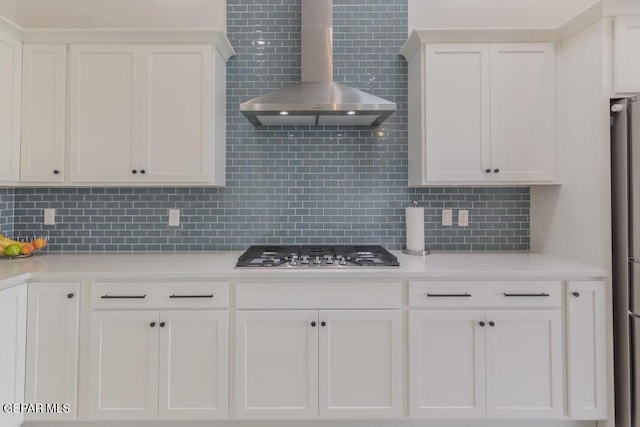 kitchen featuring decorative backsplash, white cabinetry, wall chimney range hood, and stainless steel gas cooktop