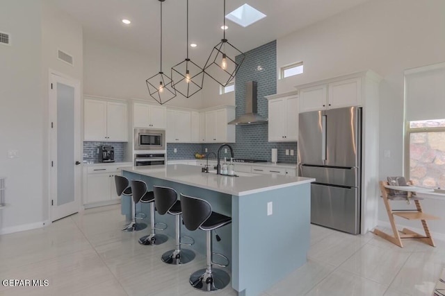 kitchen with a high ceiling, white cabinets, a skylight, wall chimney exhaust hood, and appliances with stainless steel finishes