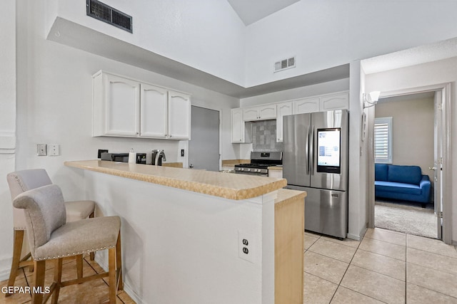 kitchen with stainless steel appliances, light tile patterned floors, kitchen peninsula, a kitchen bar, and white cabinets