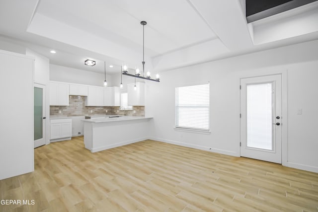 kitchen featuring kitchen peninsula, light wood-type flooring, tasteful backsplash, white cabinets, and hanging light fixtures