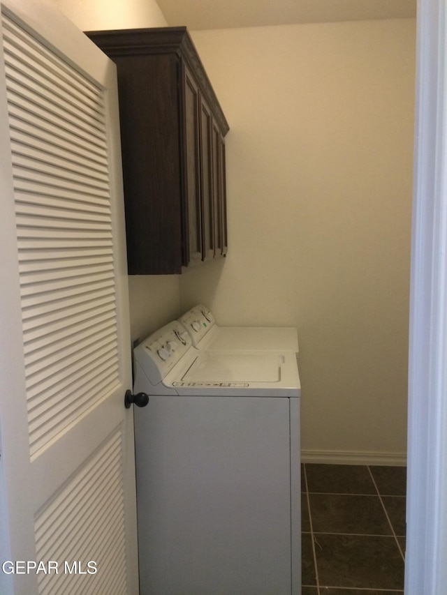 clothes washing area with dark tile patterned flooring, washer and dryer, and cabinets