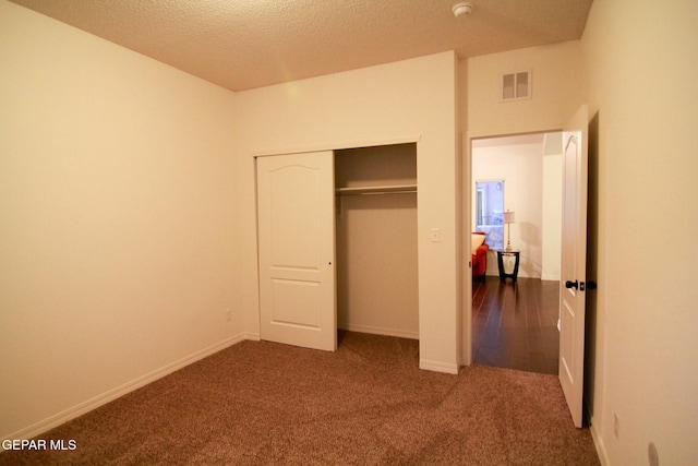 unfurnished bedroom featuring a textured ceiling, dark carpet, and a closet