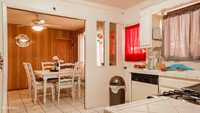 kitchen featuring white cabinetry, tile counters, white dishwasher, and wood walls