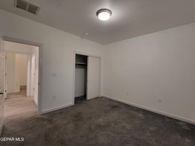 unfurnished bedroom with dark carpet and a closet