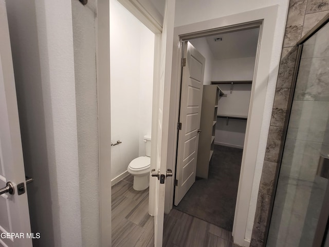 bathroom with hardwood / wood-style flooring, toilet, and a shower with shower door