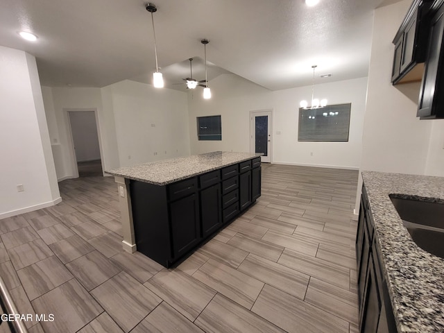 kitchen featuring light stone counters, ceiling fan with notable chandelier, vaulted ceiling, pendant lighting, and a kitchen island