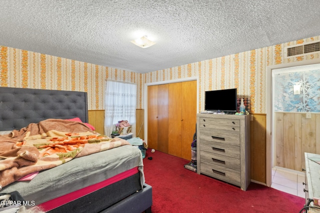 bedroom with dark colored carpet, wood walls, a textured ceiling, and a closet