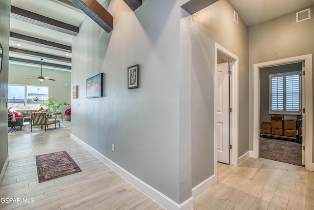 hallway featuring a healthy amount of sunlight, light wood-type flooring, beam ceiling, and a high ceiling