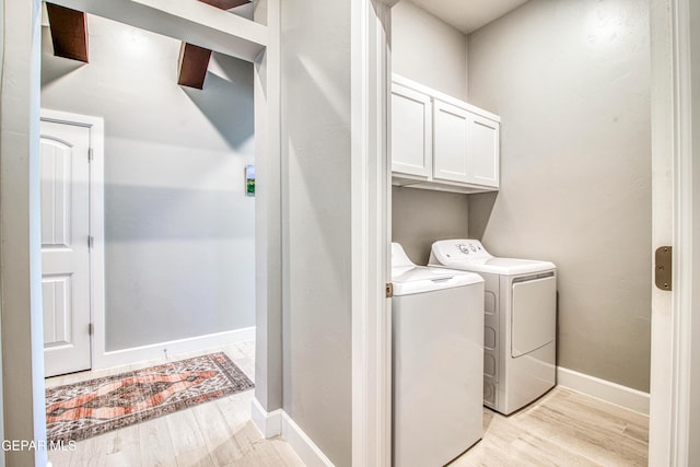 clothes washing area featuring cabinets, light hardwood / wood-style flooring, and washer and clothes dryer