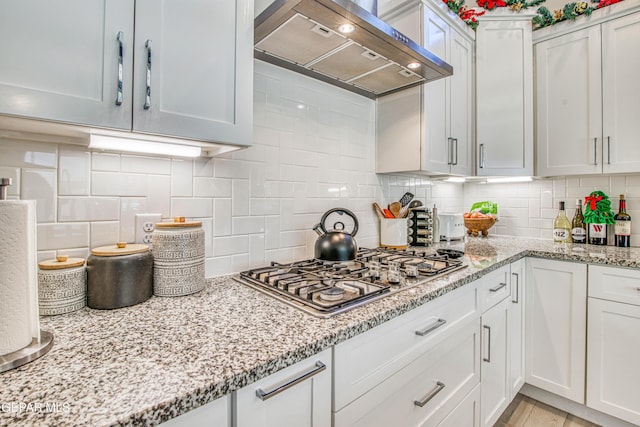kitchen with backsplash, white cabinetry, wall chimney exhaust hood, and stainless steel gas stovetop