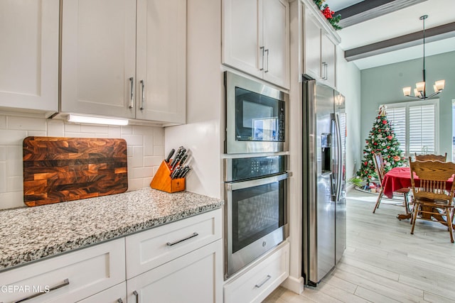 kitchen featuring white cabinetry, stainless steel appliances, a notable chandelier, backsplash, and light wood-type flooring
