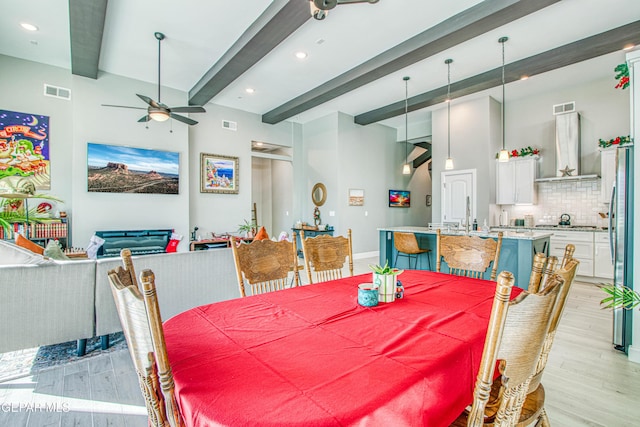 dining area featuring a fireplace, beam ceiling, light wood-type flooring, and ceiling fan