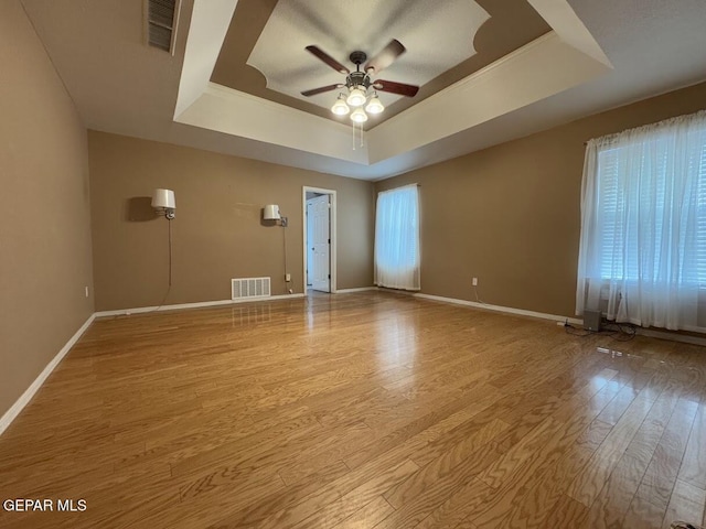 unfurnished room featuring a raised ceiling, ceiling fan, light hardwood / wood-style flooring, and a healthy amount of sunlight