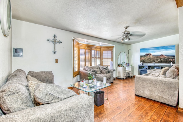 living room featuring wood-type flooring, a textured ceiling, and ceiling fan