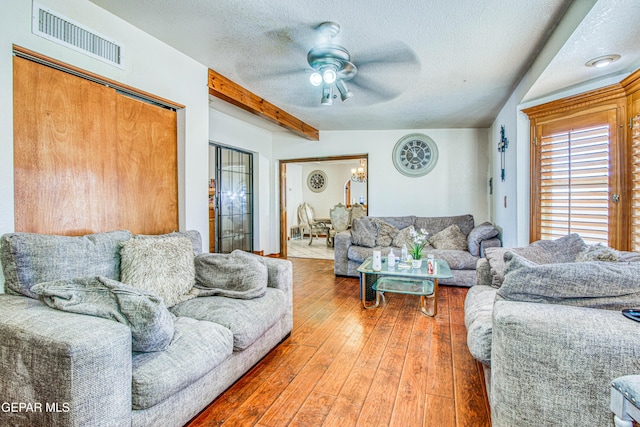 living room with ceiling fan, beam ceiling, wood-type flooring, and a textured ceiling