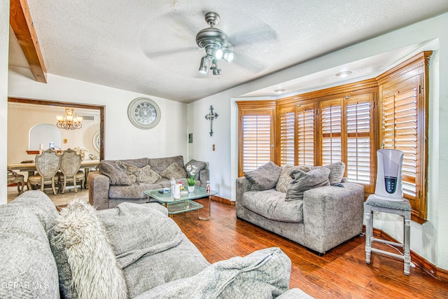 living room featuring vaulted ceiling with beams, ceiling fan with notable chandelier, wood-type flooring, and a textured ceiling