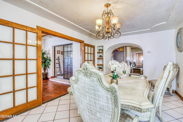 tiled dining area featuring built in shelves, a textured ceiling, and an inviting chandelier