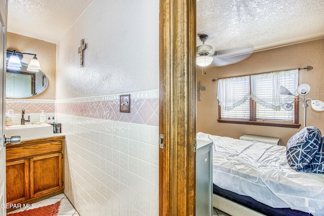 bathroom with tile patterned floors, a textured ceiling, vanity, ceiling fan, and tile walls