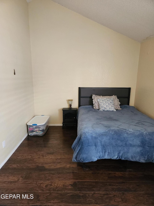 bedroom featuring a textured ceiling, dark wood-type flooring, and vaulted ceiling