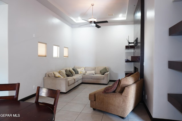 living room featuring a raised ceiling, ceiling fan, and light tile patterned flooring