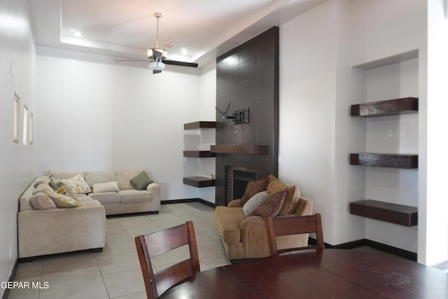 living room with ceiling fan, a tray ceiling, a fireplace, and light tile patterned floors