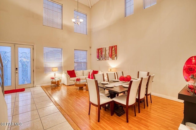 dining area with hardwood / wood-style floors, a towering ceiling, french doors, and a notable chandelier