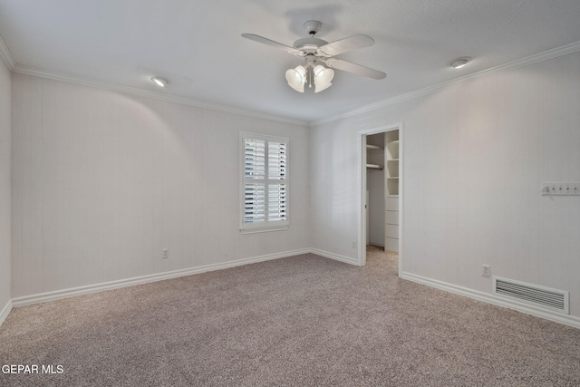 unfurnished bedroom with a ceiling fan, visible vents, carpet floors, a spacious closet, and crown molding