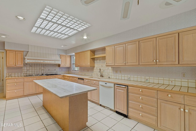 kitchen with custom range hood, light brown cabinets, white dishwasher, and a sink